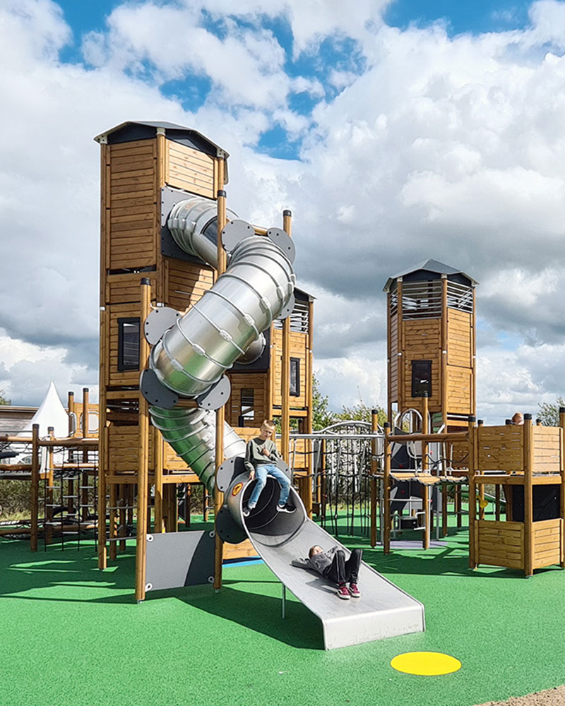 Sistema UniPlay grande y alto con muchas actividades como tobogán tubular y escalada en un parque infantil. Está hecho de madera.